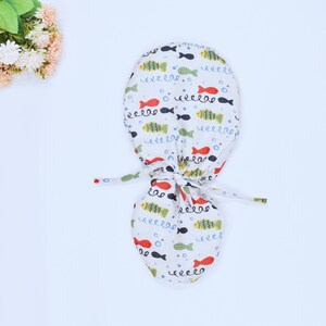 May include: A white scrub cap with a colorful fish print. The cap has a drawstring closure.