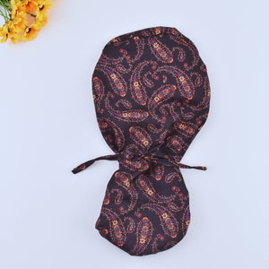 Puede incluir: Un gorro de quirófano de tela marrón con estampado de paisley y un cordón de ajuste.