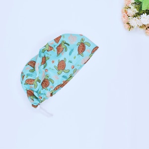 May include: A light blue surgical cap with a pattern of brown sea turtles and green seaweed. The cap has a drawstring.