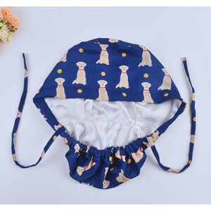 May include: A blue and white surgical cap with a pattern of yellow Labrador Retrievers. The cap has a drawstring closure and a white lining.