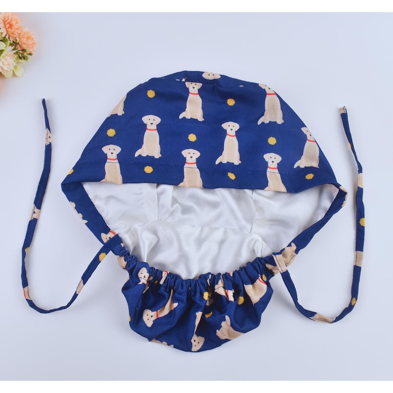 May include: A blue and white surgical cap with a pattern of yellow Labrador Retrievers. The cap has a drawstring closure and a white lining.