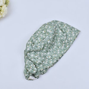Puede incluir: Un gorro quirúrgico verde claro con un estampado de margaritas blancas. El gorro está hecho de tela suave y tiene una banda elástica. Está diseñado para cubrir el cabello durante los procedimientos médicos.