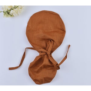 May include: A brown linen baby bonnet with ties. The bonnet is made of a soft, natural fabric and is perfect for keeping a baby's head warm and protected.