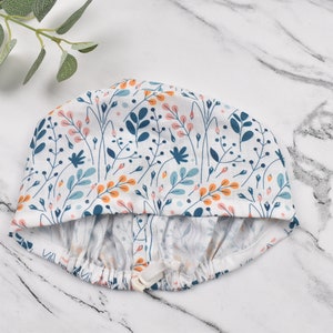 Puede incluir: Un gorro de ducha blanco con un estampado floral en tonos azules, naranjas y rosas. El gorro tiene una banda el&aacute;stica y un cierre de cord&oacute;n.