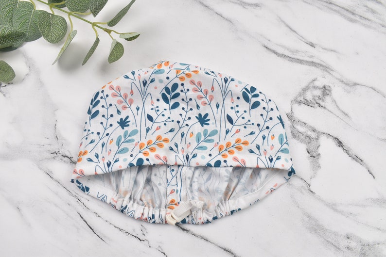Puede incluir: Un gorro de ducha blanco con un estampado floral en tonos azules, naranjas y rosas. El gorro tiene una banda el&aacute;stica y un cierre de cord&oacute;n.