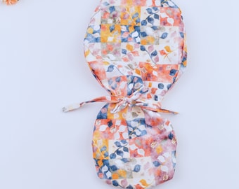 Peut inclure: Un bonnet chirurgical coloré avec un motif de feuilles et de carrés dans des tons d'orange, jaune, bleu et rose.