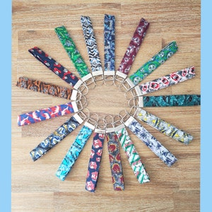 May include: A collection of 18 colorful keychains with different designs and patterns. The keychains are arranged in a circle on a wooden surface.