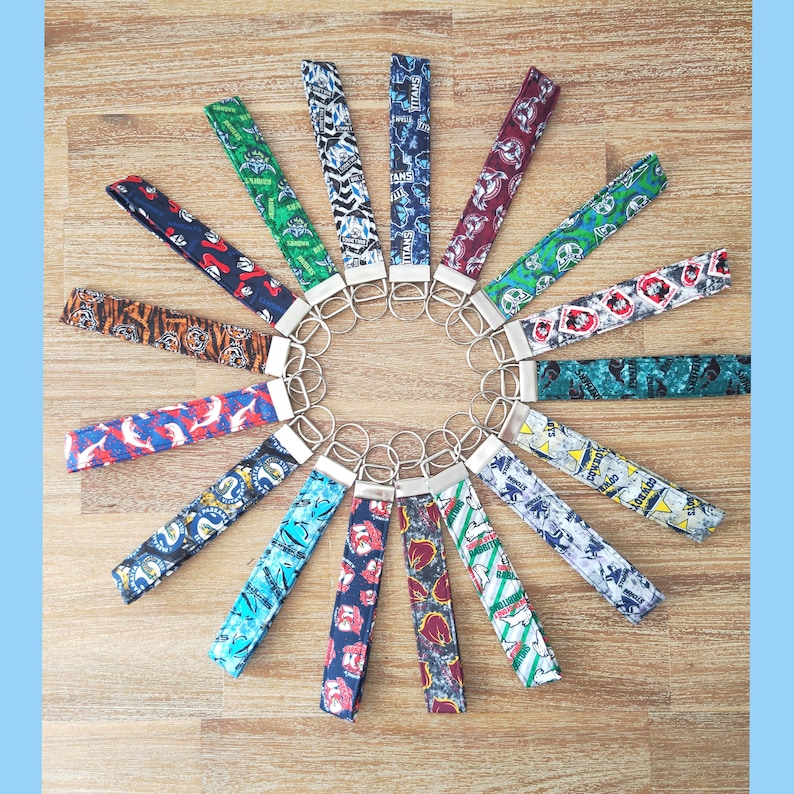 May include: A collection of 18 colorful keychains with different designs and patterns. The keychains are arranged in a circle on a wooden surface.