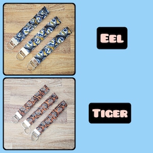 May include: Three keychains with different animal prints. The top row features three blue and white keychains with an eel print. The bottom row features three orange and black keychains with a tiger print. The word "EEL" is written in pink on a black rectangle above the top row of keychains. The word "TIGER" is written in pink on a black rectangle above the bottom row of keychains.