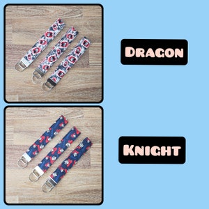 May include: Three keychains with different designs. The top keychain has a blue and red dragon design with the word "DRAGON" printed on a black rectangle. The bottom keychain has a blue and red knight design with the word "KNIGHT" printed on a black rectangle.