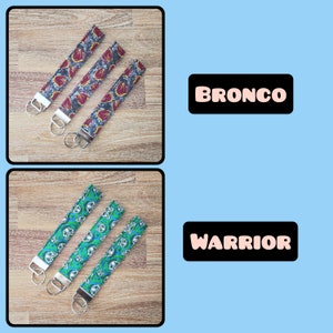 May include: Three keychains with different patterns. The top keychain has a red, white, and blue pattern with the word "BRONCO" printed on a black rectangle. The bottom keychain has a green and blue pattern with the word "WARRIOR" printed on a black rectangle.
