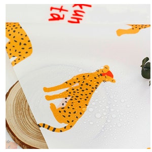 May include: White fabric with a repeating pattern of orange and black leopards. The fabric is wet with water droplets. The text "Fun at the" is visible in red.