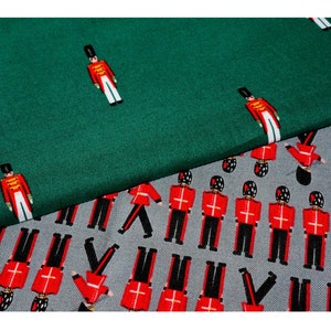 May include: Two fabric swatches with a repeating pattern of toy soldiers. The top swatch is a dark green colour and the bottom swatch is a light grey colour.