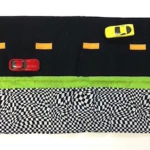 May include: A black and green fabric play mat with a checkered pattern and a road design. The mat has two toy cars, one red and one yellow, and the text "Roll N Go" on a tag.