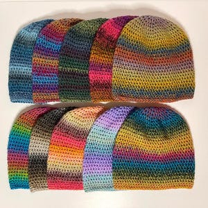 May include: A collection of ten colorful crocheted hats in various shades of blue, green, purple, pink, and yellow. The hats are stacked in two rows, with the top row slightly offset from the bottom row.
