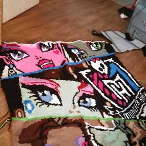 May include: A multi-colored knitted blanket with a graphic design featuring a cartoon character with large eyes and the text "Monster High".