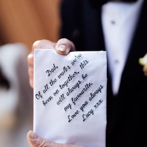 Op de afbeelding: Een wit zakdoek met handschrift in zwarte inkt met de tekst: "Papa, van alle wandelingen die we samen hebben gemaakt, zal deze altijd mijn favoriet blijven. Ik hou van je altijd Lucy xxx"