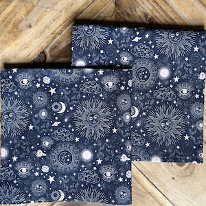 May include: Two dark blue fabric squares with a white celestial pattern. The pattern includes suns, moons, stars, planets, and eyes.