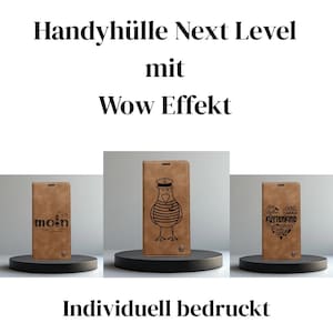 Könnte beinhalten: Drei braune Handyhüllen mit einzigartigen Designs. Eine Hülle zeigt das Wort "moin" mit einem kleinen Leuchtturm, eine andere eine nautische Möwenillustration, und die dritte zeigt Küstentext. Die Hüllen werden auf schwarzen runden Ständern präsentiert.