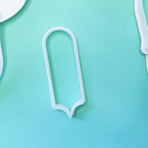 Puede incluir: Cortador de galletas de plástico blanco en forma de rectángulo con esquinas redondeadas y fondo puntiagudo.