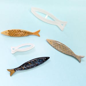 Könnte beinhalten: Drei dekorative Fisch-Ornamente, zwei mit einem braunen und weißen Muster und eines mit einem blauen und schwarzen Muster. Die Fische sind aus Keramik oder Glas und haben eine glänzende Oberfläche.