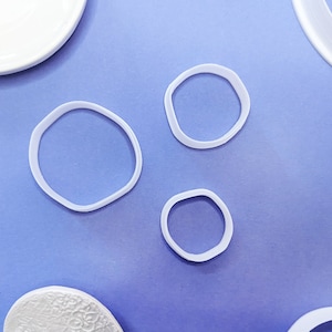 Könnte beinhalten: Vier weiße Plastik-Ausstecher auf einem violetten Hintergrund. Die Ausstecher haben die Form von Kreisen und Ovalen.