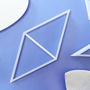 May include: A set of white plastic geometric shapes, including a diamond, a triangle, and a square, on a light purple background.