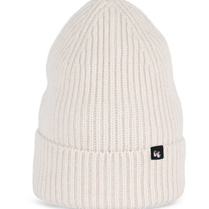 A very light ivory beanie with chunky, fisherman-style ribbed knit. It has a black fabric label with a white logo stitched to the cuff