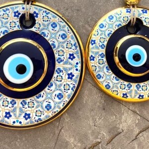 May include: Two round blue and white evil eye wall decor with gold trim. The larger evil eye is surrounded by a white and blue patterned design.