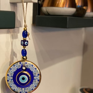 May include: A blue and white ceramic evil eye charm with gold trim and a beaded string hanging from a hook.