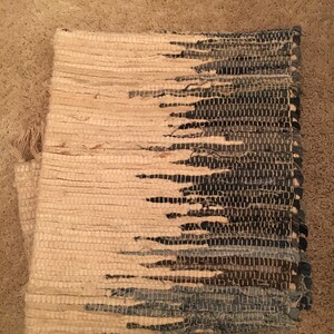 May include: A woven rug with a gradient design. The rug is made of natural fibers and has a light beige color on one side and a dark blue color on the other side.