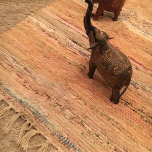 May include: Two wooden elephant figurines on a woven rug. The elephant on the left is black with intricate carvings and its trunk is raised. The elephant on the right is brown and its trunk is down.