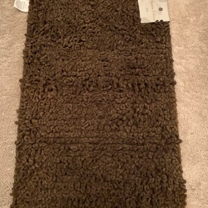 May include: A brown bath mat with a textured surface. The mat has a white tag with the text "Signature Collection" and "700g" on it.