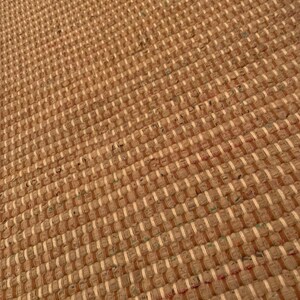 May include: A close-up of a woven rug with a brown and white checkered pattern. The rug is made of natural fibers and has a rustic look.