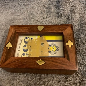 May include: A wooden frame with a glass front, displaying two playing cards. The frame is decorated with brass accents in the shape of a heart, diamond, and two clubs.