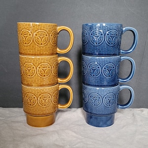 以下が含まれることがあります： 幾何学模様の入った青いセラミックマグカップ4個と茶色のセラミックマグカップ4個のセット。マグカップは積み重ねられています。