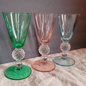 May include: Three stemmed drinking glasses with a golf ball design on the base. The glasses are green, pink, and blue.