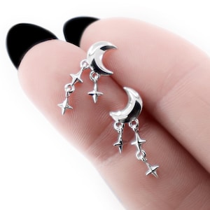 Könnte beinhalten: Silberfarbene Ohrringe mit einem Mond-Design und hängenden Sternen. Die Ohrringe haben eine polierte Oberfläche und sind für durchbohrte Ohren konzipiert. Der Schmuck mit Himmelsmotiven ist ein zartes und stilvolles Accessoire.