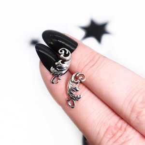 Könnte beinhalten: Ein Paar silberne Ohrringe mit einem zarten, verzierten Design. Die Ohrringe sind in Form eines stilisierten Blattes oder einer Feder geformt.