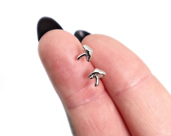 May include: A pair of small, silver-toned mushroom-shaped stud earrings. Each earring features a detailed cap with etched lines and a slender stem, crafted in a polished metallic finish. These tiny accessories are designed for earlobe placement.