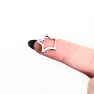 May include: A small, silver-colored star-shaped earring. The earring is a simple, open design, with five points. The earring is shown against a white background.
