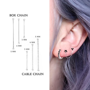 Può includere: Catene a scatola e catene a maglia forzatina in lunghezze da 3 mm, 4 mm e 5 mm sono mostrate accanto a un orecchio con un cerchio argentato con pietre nere, un perno a forma di stella e una doppia catenella che collega la stella a un piccolo perno.