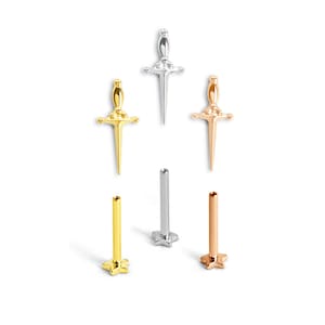 Op de afbeelding: Een assortiment kleine, metalen sieraden in de vorm van dolken en sterren. De dolken zijn in goud, zilver en roségoud. De ster-vormige stukken zijn in goud, zilver en roségoud. De sieraden staan op een witte achtergrond.