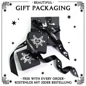 May include: Black gift boxes with white starburst designs and the text "STAY REBEL" are tied with black satin ribbons. The ribbons have white text and celestial designs. The words "BEAUTIFUL GIFT PACKAGING" are at the top.