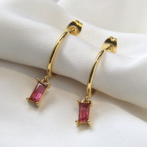 Peut inclure: Boucles d'oreilles créoles dorées avec une pierre rectangulaire rose pendante.
