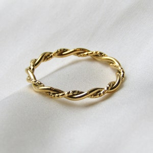 May include: A gold-toned twisted band ring. The ring is made of a thick, braided metal.