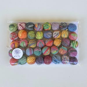 May include: A package of 40 small yarn balls in various colors, including green, orange, blue, and purple. The yarn balls are tightly wound and displayed in a clear plastic bag. The package has a round sticker with text.