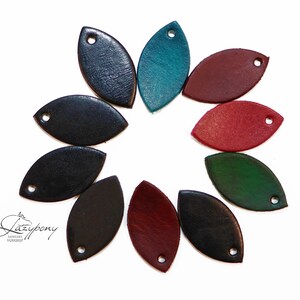 Puede incluir: Una colección de diez dijes de cuero con forma de hoja dispuestos en círculo. Cada dije presenta un orificio en un extremo y viene en varios colores, incluyendo negro, azul oscuro, turquesa, rojo, rojo oscuro y verde. El texto Lazypony es visible.