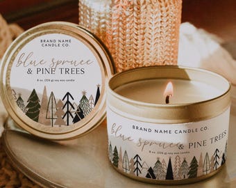 Może przedstawiać: Zapalone świeca w puszce ze złotą obwódką z napisem "Blue Spruce & Pine Trees". Świeca stoi na srebrnym talerzu, obok pasującej pokrywki. Tło obejmuje dekoracyjny wazon i tkany podkładka. Świeca ma 226g.
