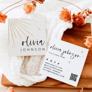 May include: Two square business cards with the name "Olivia Johnson" in elegant script. One card features a sunburst design, while the other includes contact details and a QR code. Dried orange flowers and a wooden tray complete the aesthetic.